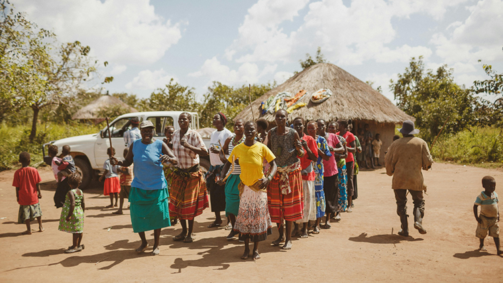 A group of African women dancing in a rural village, wearing colorful skirts and celebrating with music.